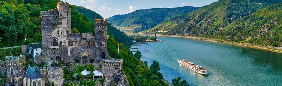 Burg Rheinstein castle overlooking the Rhine Gorge in Germany with a river cruise ship sailing below