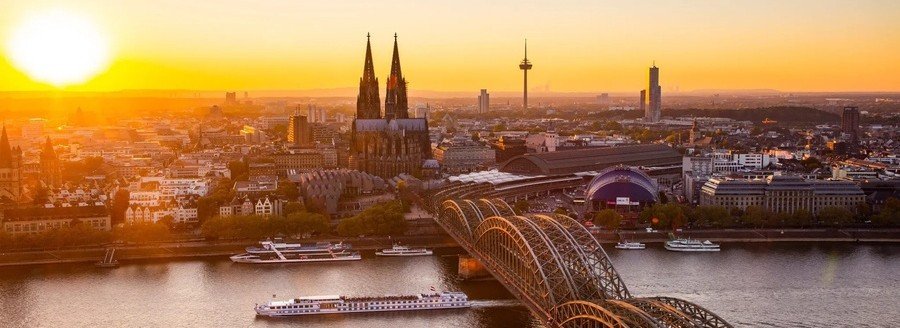Cologne Cathedral and Hohenzollern Bridge at sunset along the Rhine River with a river cruise ship in Germany