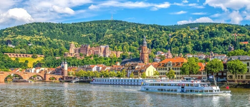 Heidelberg Castle overlooking Old Town rooftops and a river cruise boat on the Neckar River in Germany
