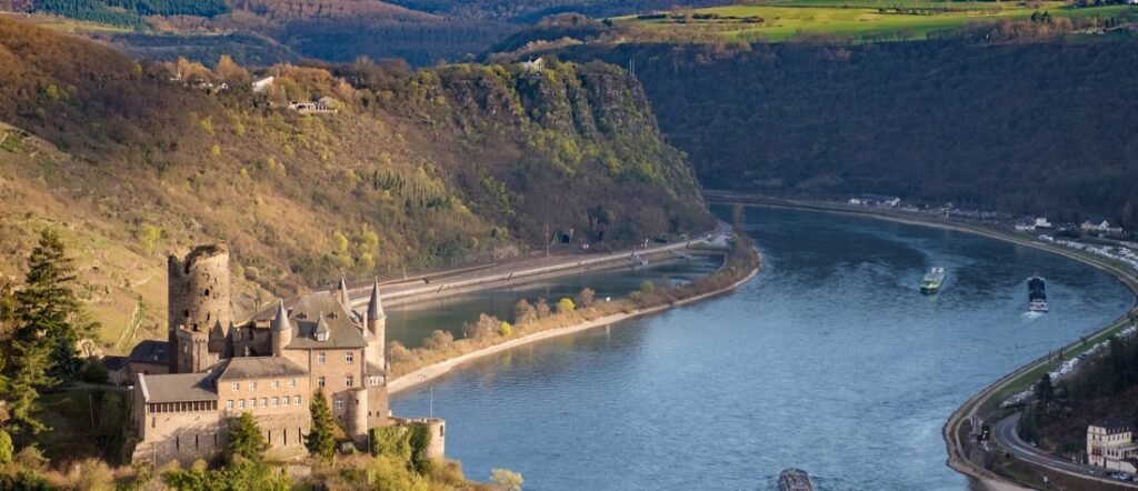 Rhine Gorge castle overlooking the Rhine River with cruise ships sailing through the UNESCO Upper Middle Rhine Valley in Germany